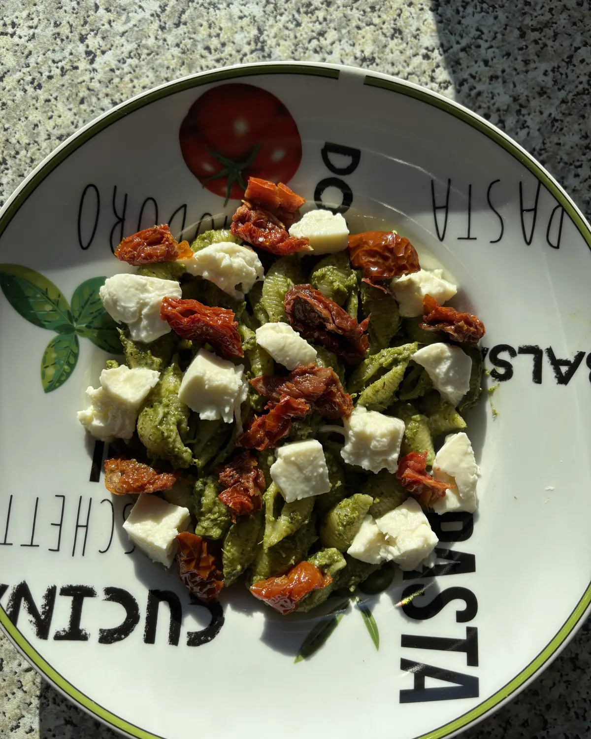Assiette de pâtes au pesto vert avec des dés de feta et des tomates séchées