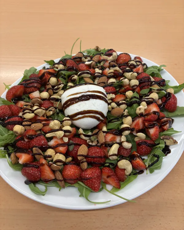 Assiette de roquette avec des fraises coupées, une burrata, des noix et un filet de vinaigre balsamique