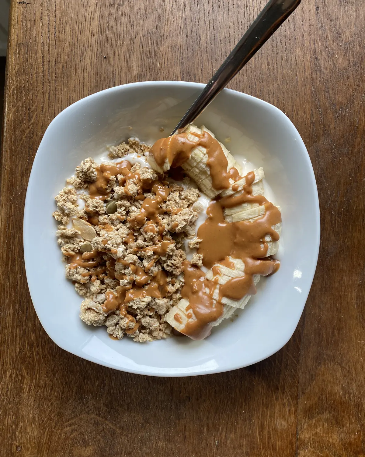 Bol de yaourt garni de granola, de rondelles de banane et d'un filet de beurre de cacahuète