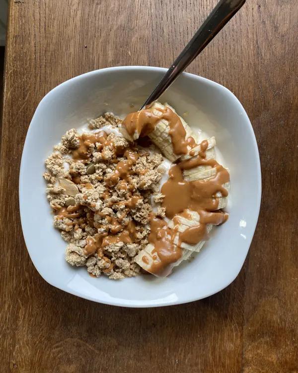 Bol de yaourt garni de granola, de rondelles de banane et d'un filet de beurre de cacahuète